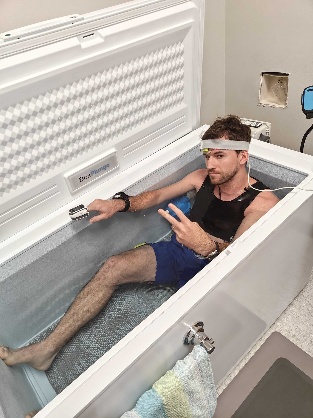 Thibault sitting in a cold-water immersion tub wearing a forehead band and chest sensors. Cold-water immersion with a forehead band and chest sensors.