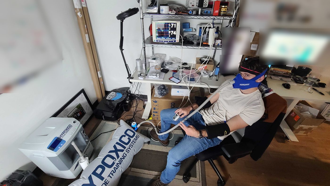 Thibault seated in the lab breathing through a blue mask connected to an altitude generator, with a sensor headband and a clinical monitor. Hypoxia test with an altitude generator, forehead sensors and a reference clinical monitor.