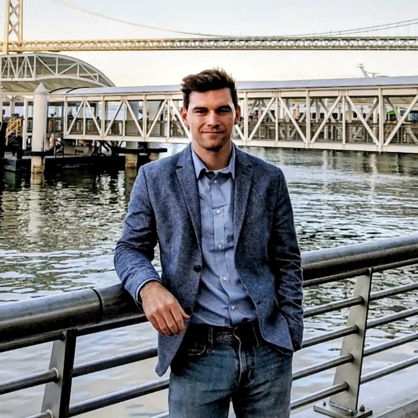 Thibault Roumengous standing by the water in San Francisco with the Bay Bridge behind him